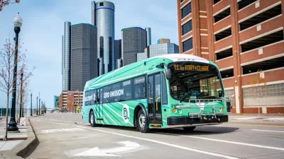 Green Detroit public transit electric bus with high-rise modenr building in background.