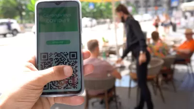 A digital vaccination record appears on a smartphone in front of a blurred background showing diners in an outdoor setting.