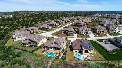 A subdivision of large suburban homes, some with bright blue pools, sits atop a low hill in Hays County, Texas.