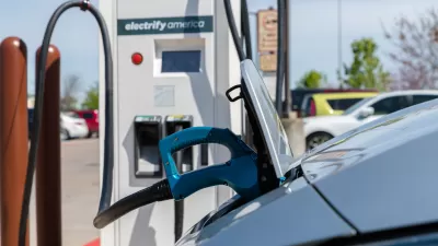 An electric vehicle is plugged into a charging station. A sticker reads “charge America” on the station.