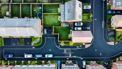 A suburban street in England, shown directly from above, with lush, green yards and driveways with cars parked in front.