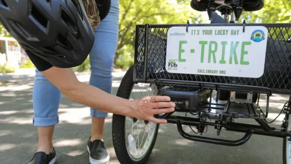 Close-up of person putting sticker on back of basket of electric tricycle with mock license plate reading "E-TRIKE."
