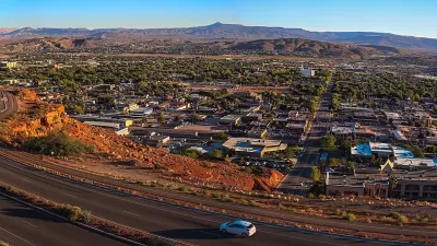 Aerial view of St. George, Utah at sunset with road in foreground and red mountains in background.