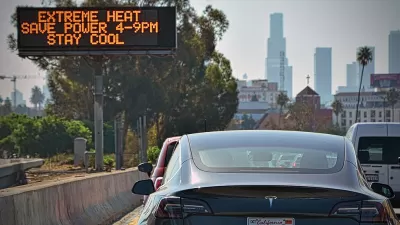Cars in traffic jam on Los Angeles highway with road sign in center median warning of extreme heat.