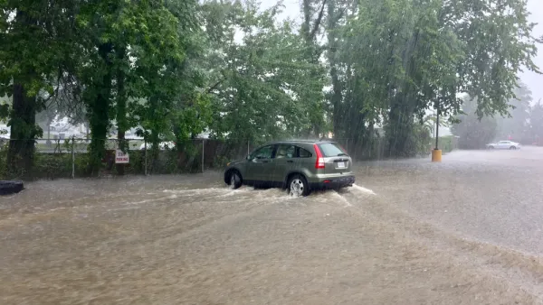 A sports utility vehicle drives throw brown floodwaters that have inundated the entire area depicted in the picture.
