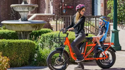 Woman in purple helmet on orange e-bike with baby in seat on back of bike.