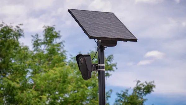 Close-up on black Flock surveillance license plate reader camera with solar panel.