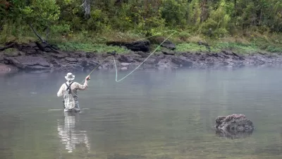 A fly fisher casts on a fog-covered river.