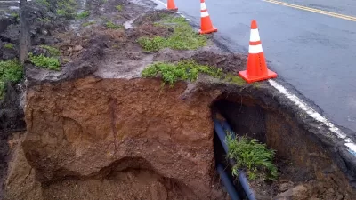 Eroded cliffside and exposed utilities along asphalt Highway 1 in California with orange traffic cones lining side of road.