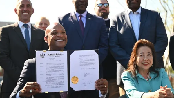 Governor Wes Moore of Maryland holds up executive order while sitting at table surrounded by smiling officials.