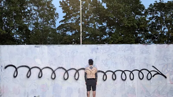 Man standing in front of white wall with black graffiti paint spiral running horizontally across.
