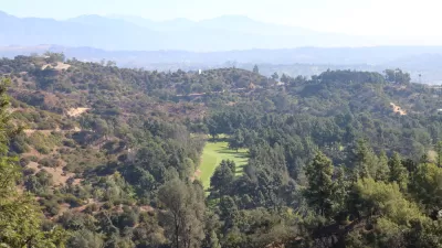 The fairway of a golf course is visible amidst the rolling hills of Griffith Park above Los Angeles.