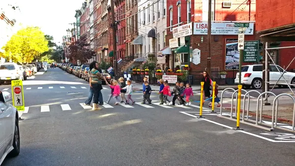 Group of children with crossing guard crossing the street at a marked crosswalk in Hoboken, New Jersey on street with brick walk-up buildings.