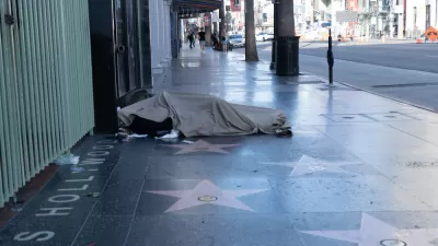 A person experiencing homelessness sleeps on the sidewalk, atop the stars on the Hollywood Walk of Fame.