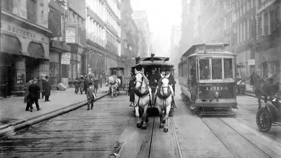 A black-and-white photo of a team of white horses pulling a trolley car along a track on a New York City Street, facing the camera.