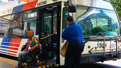Man in wheelchair exiting public bus on ramp while operator waits outside in Houston, Texas.