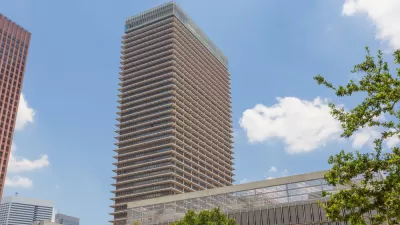 A high-rise building is seen fromt he ground, framed by an assortment of tall and shorter buildings.