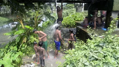 A group of young men and boys gather under water dripping from a water pipe in India.