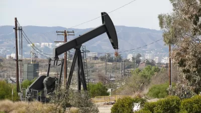 An oil well is pictured with buildings in the city of Los Angeles in the background.