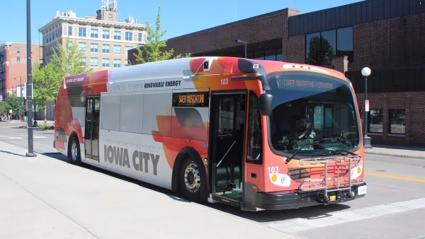 Red and white Iowa City Transit bus stopped next to a curb.