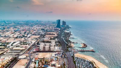 An aerial view down the length of the Jeddah coastline in Saudi Arabia, showing coastal developments, beaches, and a few high-rise buildings along the shoreline.