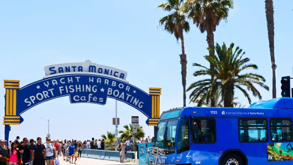Blue transit bus passing in front of Santa Monica Pier entrance arch on a sunny day.