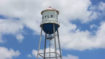 White water tower with KYLE text against blue sky with white clouds.