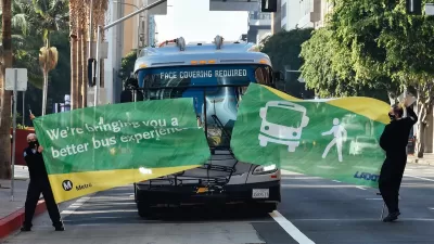 Bus driving through green banner held by two Metro employees at inauguration of new bus lane in downtown Los Angeles.