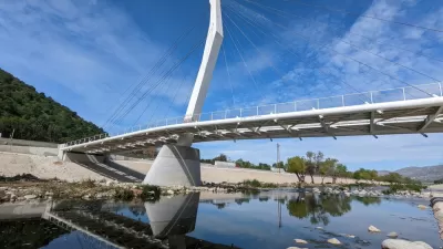 A cable-stayed bridge designed spans the water of the Los Angeles River, which is placid and dotted with rocks.