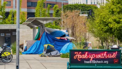A homeless encampment is set up outside a transit station, next to bike share stations and a ticket dispenser.