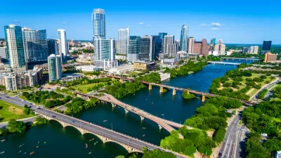 Downtown Austin with Lady Bird Lake in the foreground. Multiple bridges are crossing the lake and small personal water-crafts dot the water.