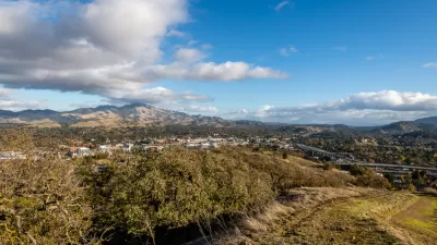 A broad valley with two tall peaks in the background. In the foregound, but far below the view from the hill where the photo was taken, large freeways are visible.
