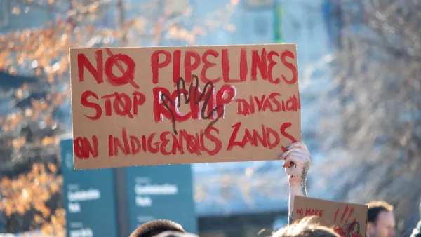 A sign held above the crowd at a protest reads "No Pipelines" and "Stop RCMP Invasion on Indigenous Lands" 