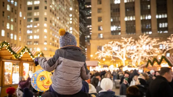 Child on adult's shoulders looking at warm holiday lights display.