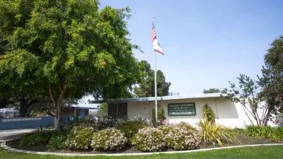 Small white one-story building with Maggie Hathaway Golf Course sign with American flag on flagpole and green lawn
