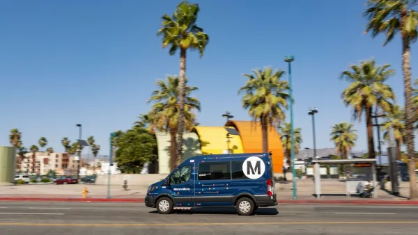 Dark blue shuttle van driving past colorful orange and yellow North Hollywood subway station in Los Angeles, California.