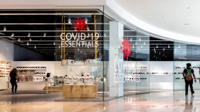 A man passes by a store in an empty mall. A sign in the window of the store reads "Covid-19 Essentials."