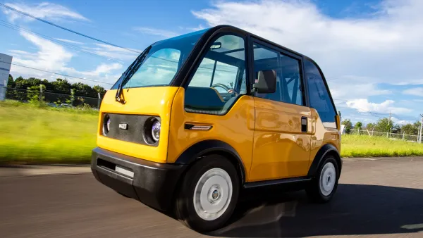 Yellow single-seat Japanese electric vehicle drivign down road.