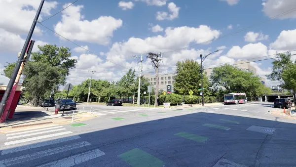 A gray building partially obscured by trees, behind a four way intersection.