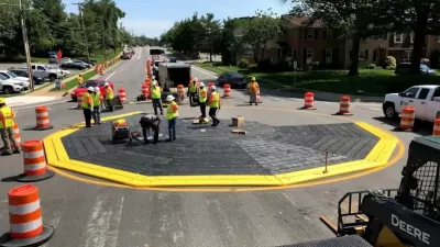 Workers in safety vests installing a black modular roundabout ringed with yellow.