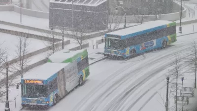 Two buses pull up to a station on a snowy day.