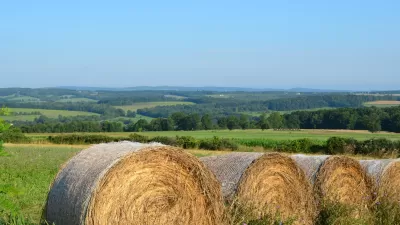 A bale if hay is rolled up in an expansive agricultural landscape.