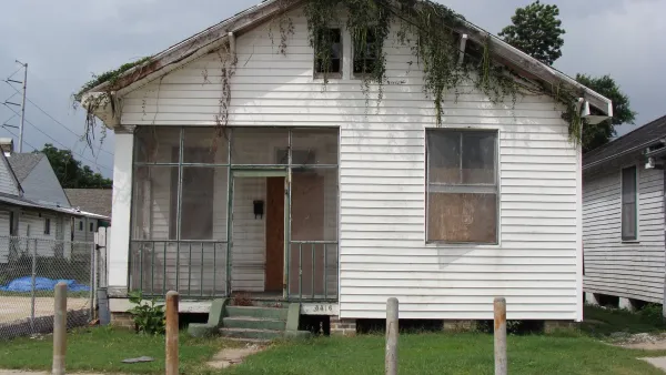 Small white wood house with boarded up windows in New Orleans, Louisiana with moss growing down from roof.