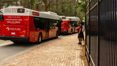 A line of buses on campus at North Carolina State University, pictured with fall leaves on the ground.