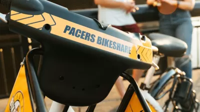 Close-up of yellow Pacers Bikeshare e-bike parked outdoors with blurred people in background.
