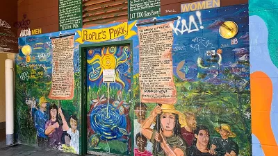 Colorful mural depicting people holding signs with proclamations on exterior wall of public restroom in People's Park, Berkeley