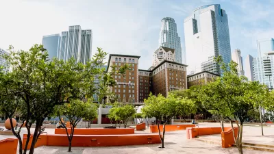 A hardscaped park with creative architectural featues is shown with the high-rises of Downtown Los Angeles in the background.