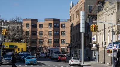 Large silver pole on street corner in LA, nearly same height as surrounding three-story buildings.