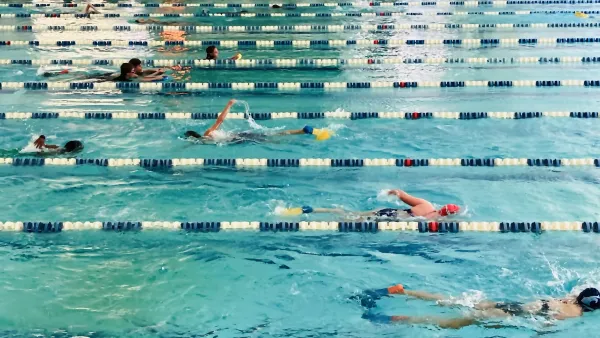 People swimming in an indoor lap pool with blue and white lane dividers.