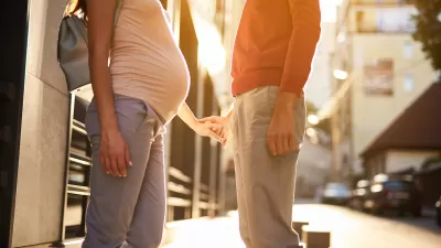 A pregnant woman holds hand with a man in an urban setting.